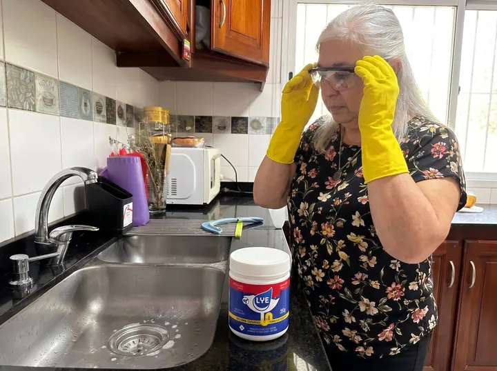 Persona poniéndose anteojos de seguridad con guantes amarillos, junto al pote Lye Clean