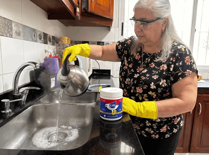 Persona con guantes volcando agua caliente desde una pava en la pileta